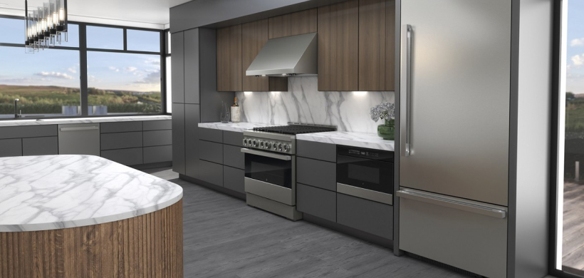 Une cuisine avec de grandes fenêtres avec vue sur le paysage. On voit une cuisinière et une hotte de cuisine JennAir, un four à micro-ondes JennAir, un lave-vaisselle JennAir et un îlot avec une surface en marbre. Sur le comptoir se trouve une plante en pot.